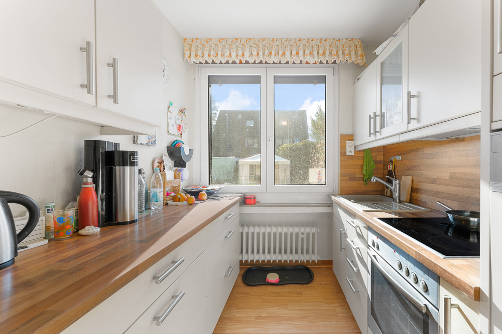 Helle Küche mit Holzarbeitsplatten, Herd, Spüle und großem Fenster mit Blick nach draußen.