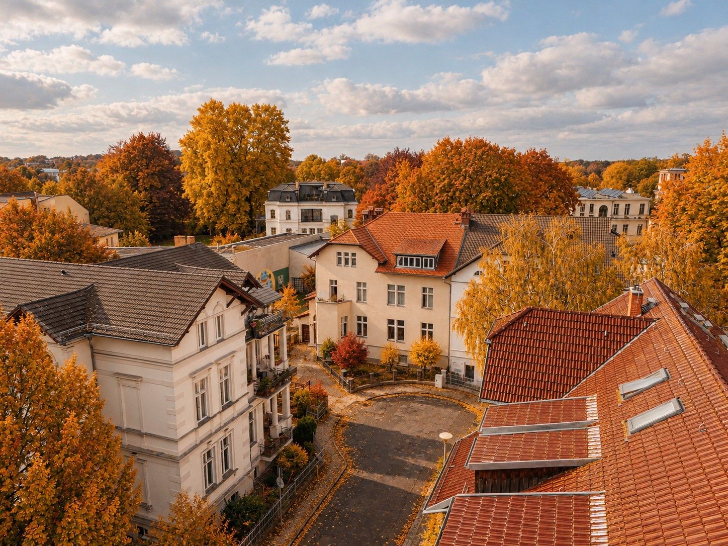 Wohnhäuser mit roten Dächern und bunten Herbstbäumen in einer ruhigen Wohngegend.