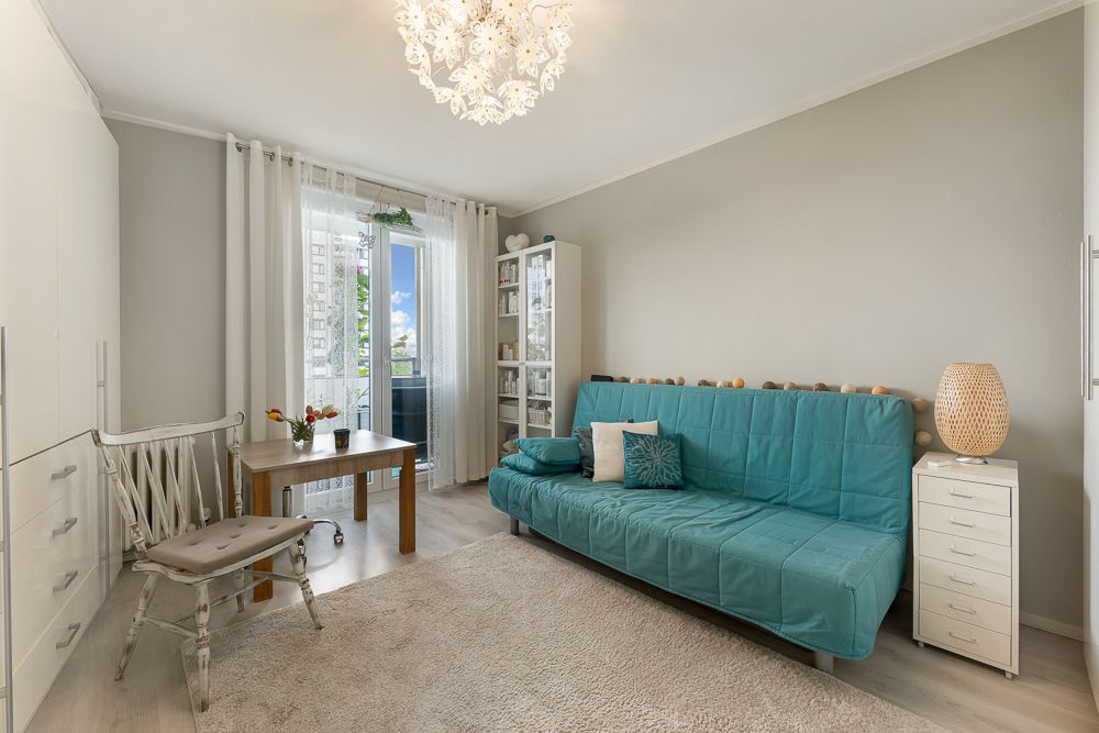 Helles Wohnzimmer mit blauem Sofa, Holztisch, Stuhl, Teppich und Balkonzugang.