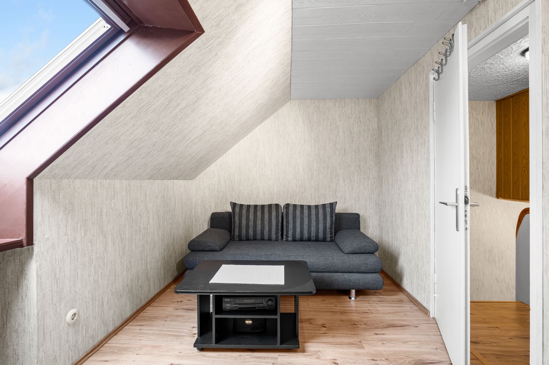Gemütliche Sitzecke mit grauem Sofa und Couchtisch unter einem Dachfenster.