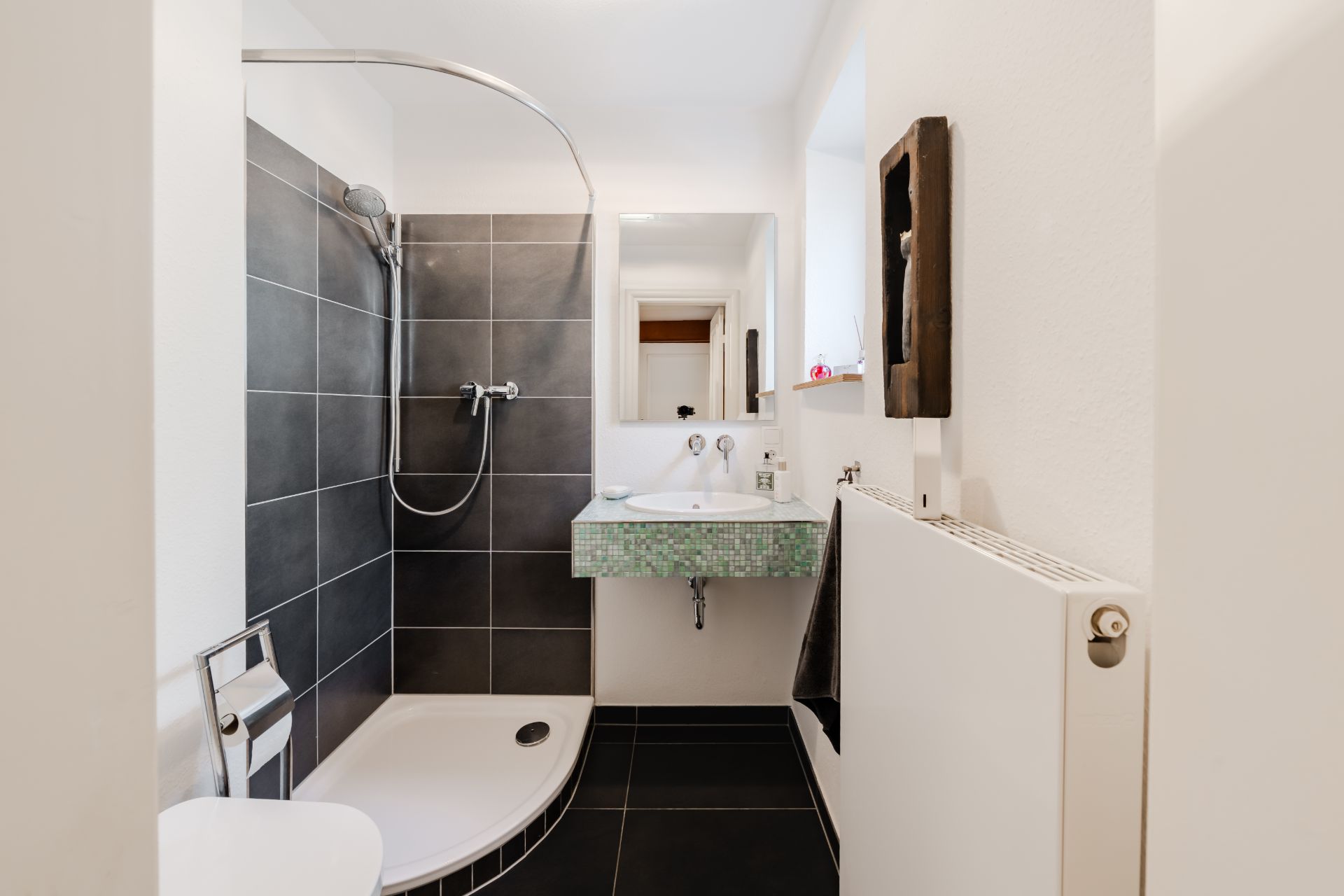 Modernes Badezimmer mit offener Dusche, Wandwaschbecken, Spiegel und WC.