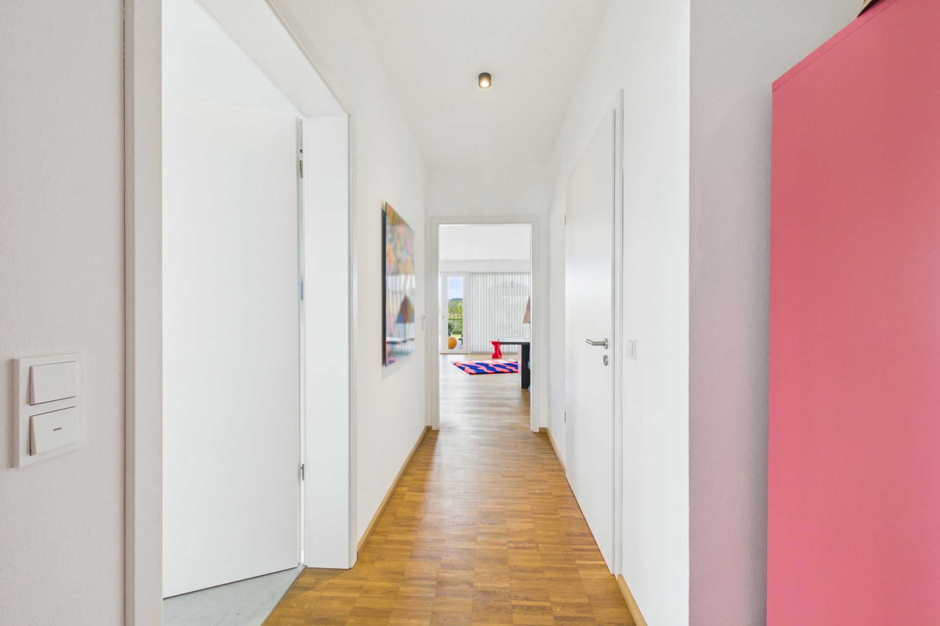 Heller Flur mit Holzboden, weißen Wänden und bunter Kommode, Türen führen in weitere Zimmer.
