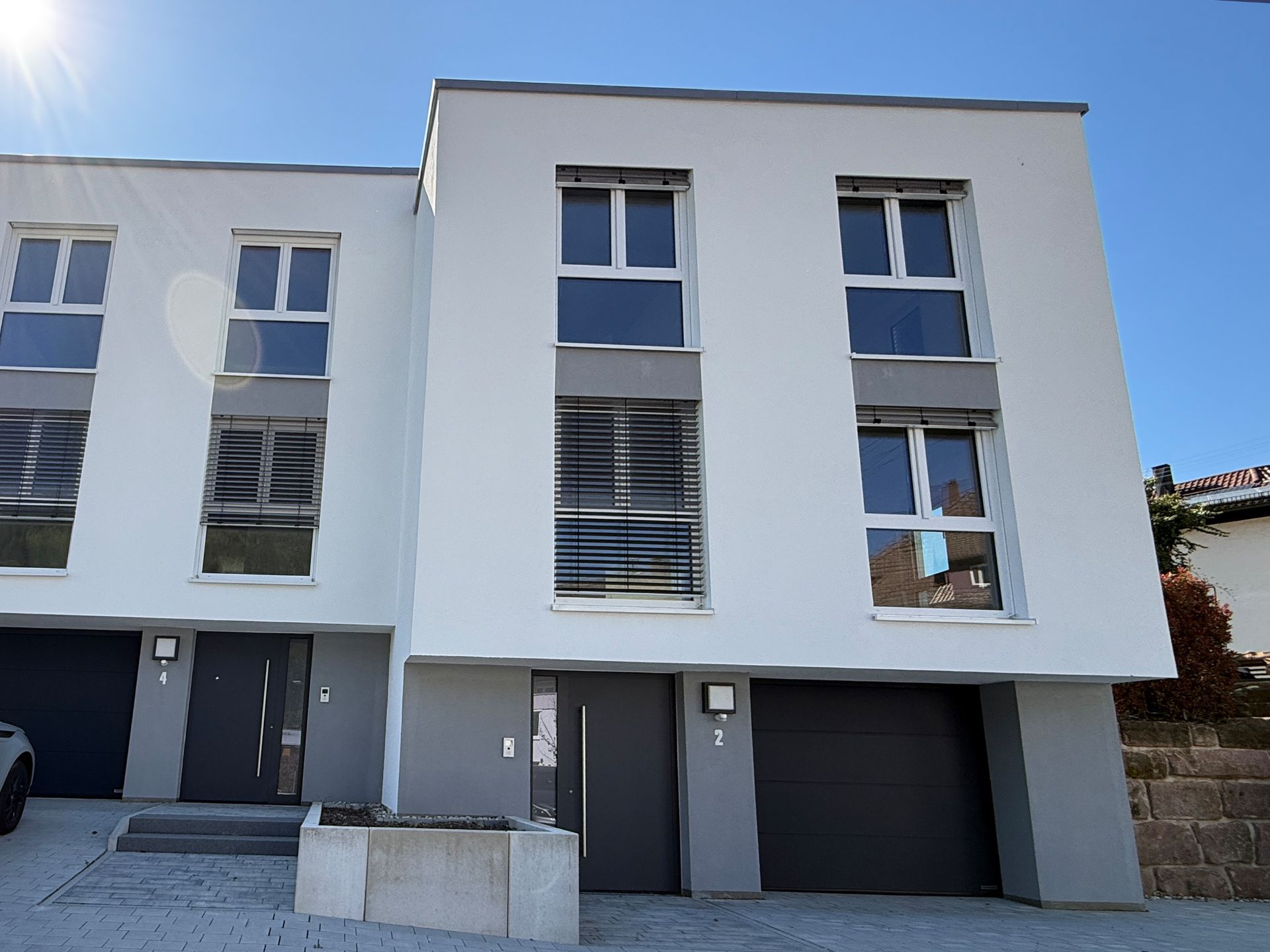 Modernes, weißes Reihenhaus mit großen Fenstern und Garage bei sonnigem Wetter.