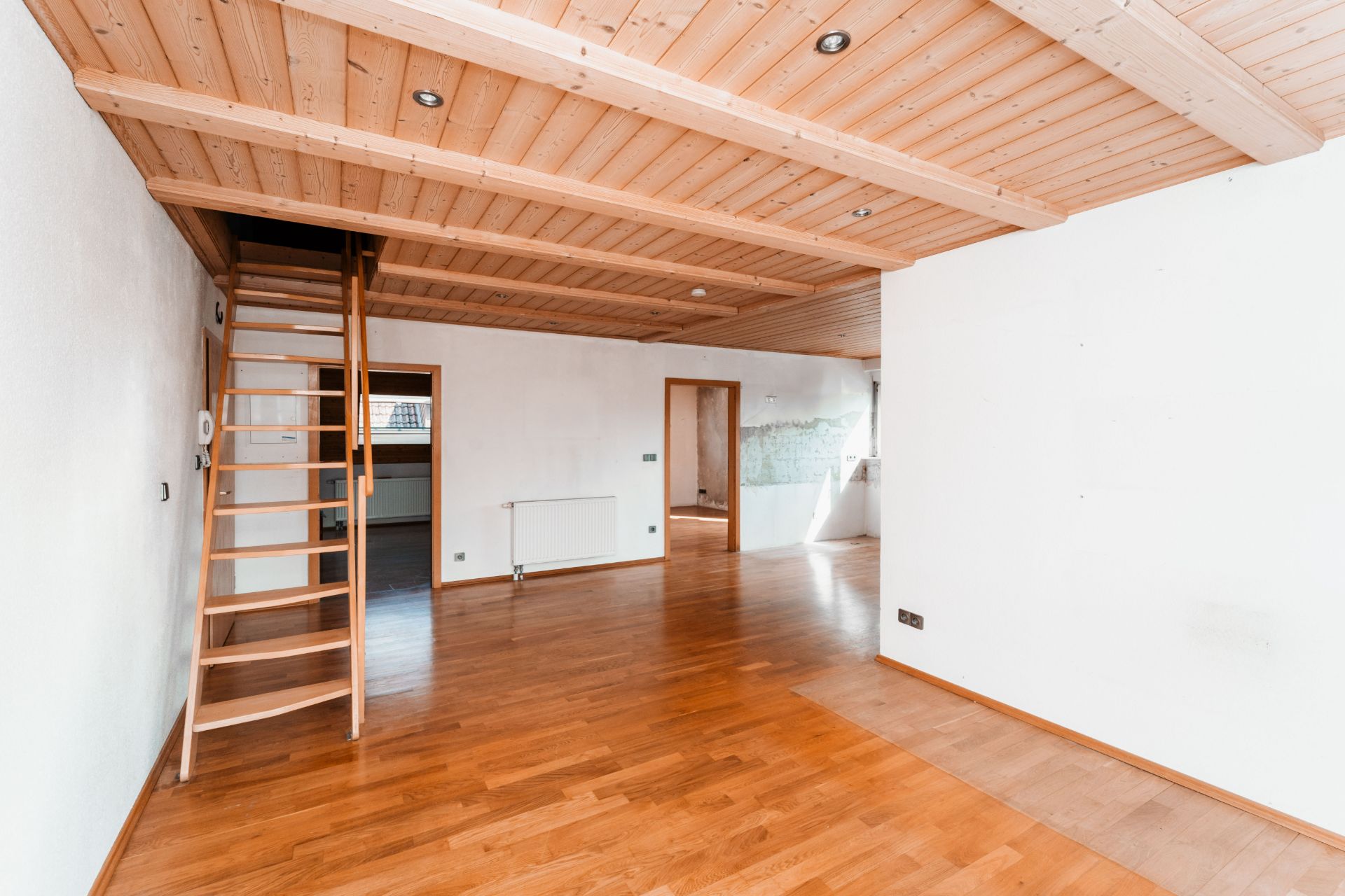 Helles Zimmer mit Holzboden, Holzdecke und einer Holztreppe zu einer Galerie.