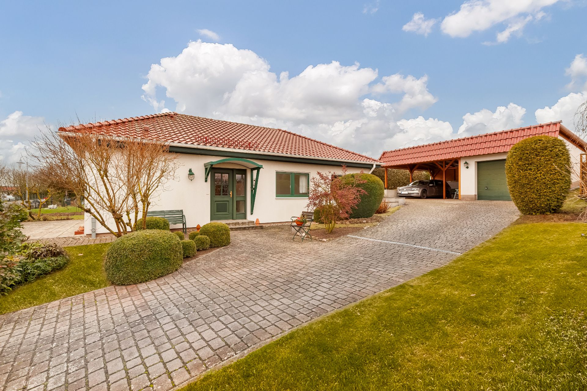Einfamilienhaus mit rotem Dach, Vorgarten und Einfahrt mit Carport und Garage.