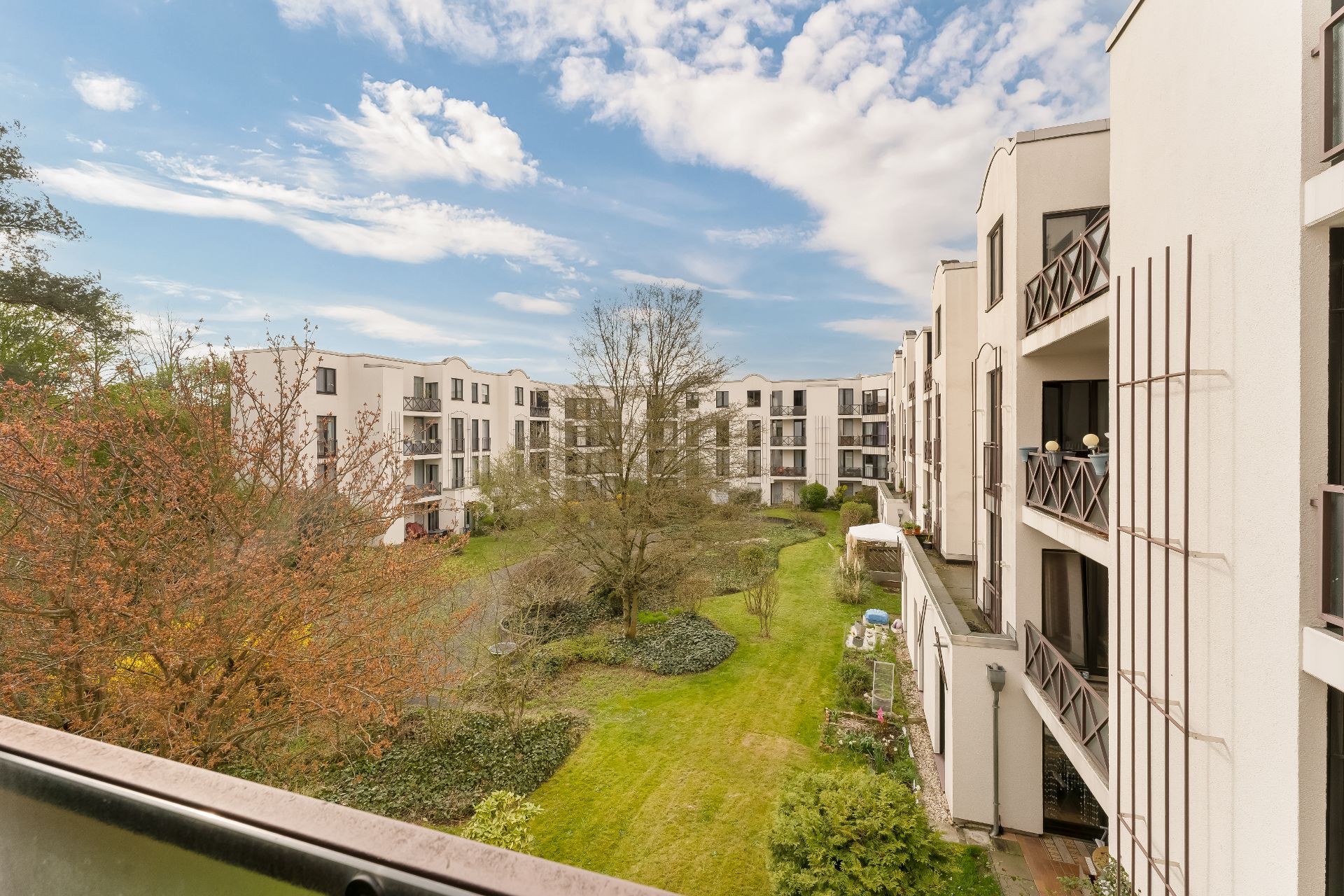 Blick auf einen Innenhof mit Grünfläche, Bäumen und modernen Wohngebäuden mit Balkonen.
