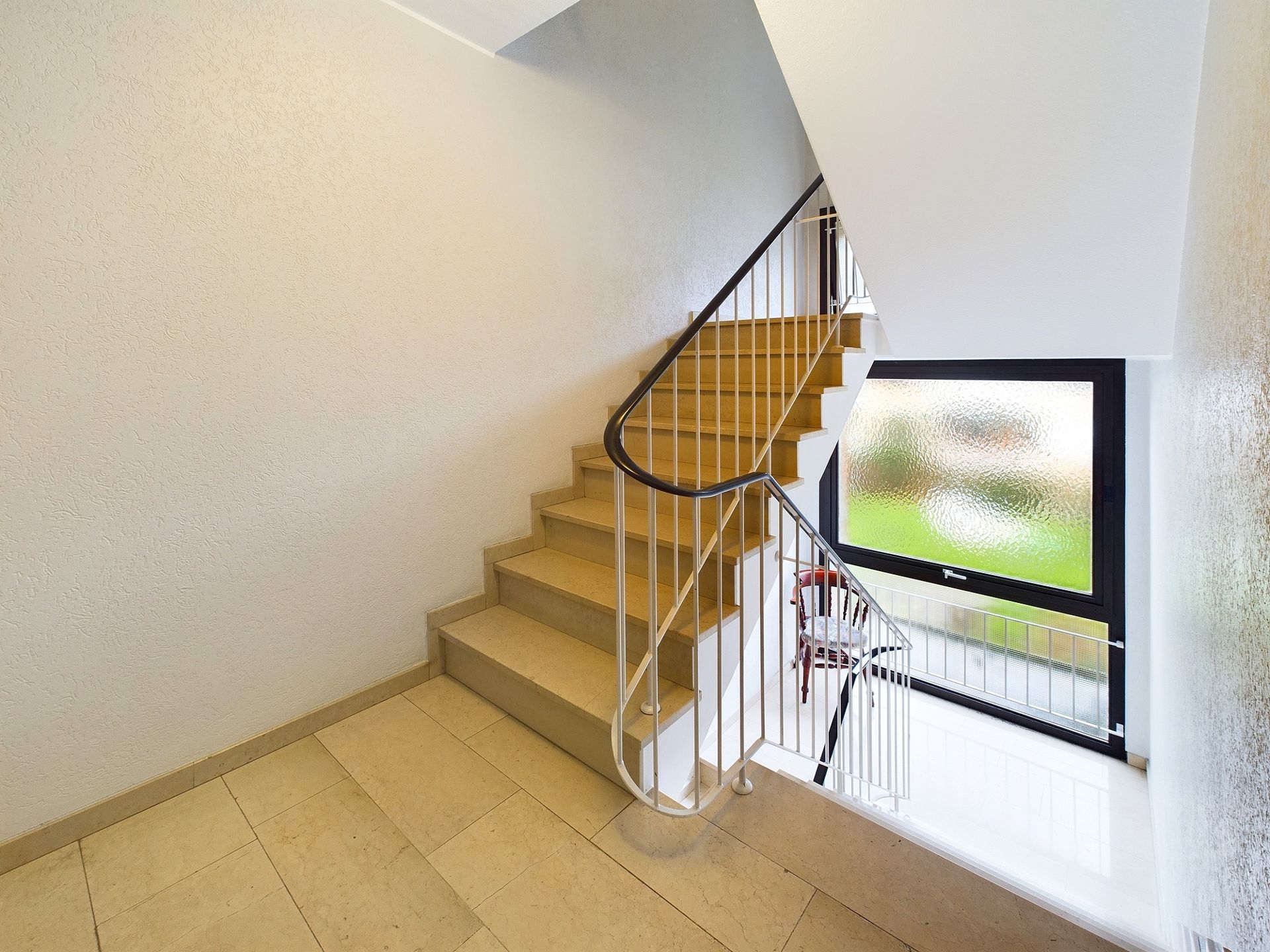 Helles Treppenhaus mit Stufen, Geländer und großem Fenster.