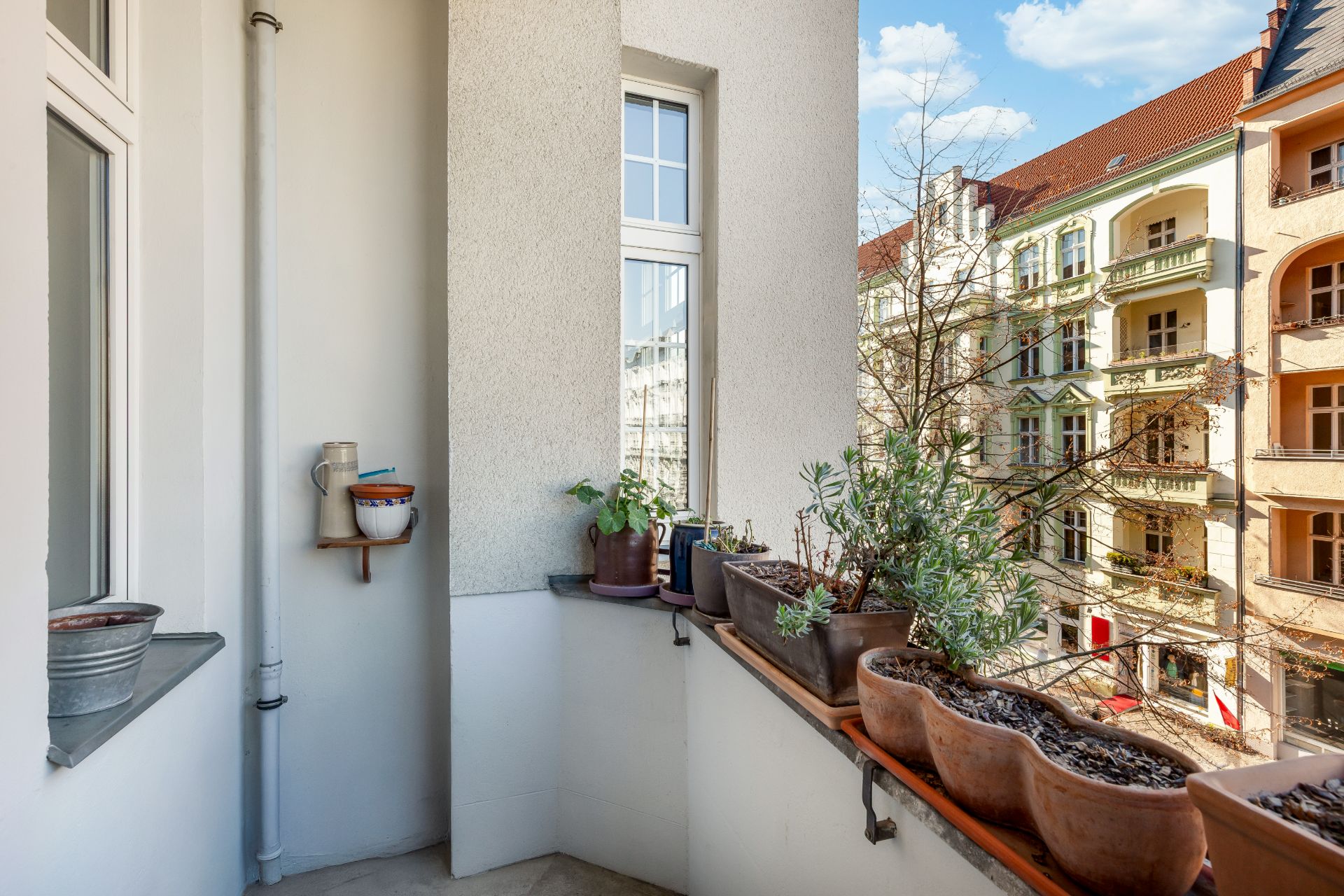 Kleiner Balkon mit Blumenkästen und Blick auf eine Wohnstraße mit Altbauten.