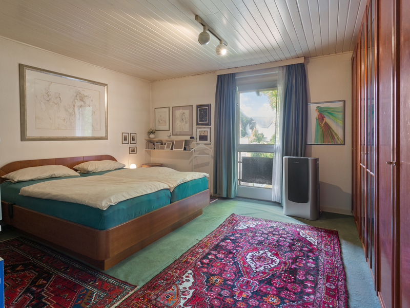 Schlafzimmer mit Doppelbett, buntem Teppich, Holzmöbeln und Fenster mit Vorhängen.