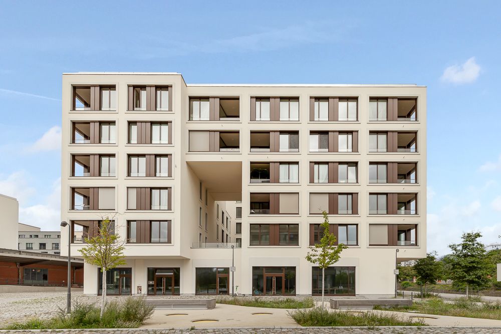 Moderne, mehrstöckige Wohnanlage mit vielen Fenstern und kleinen Bäumen davor.