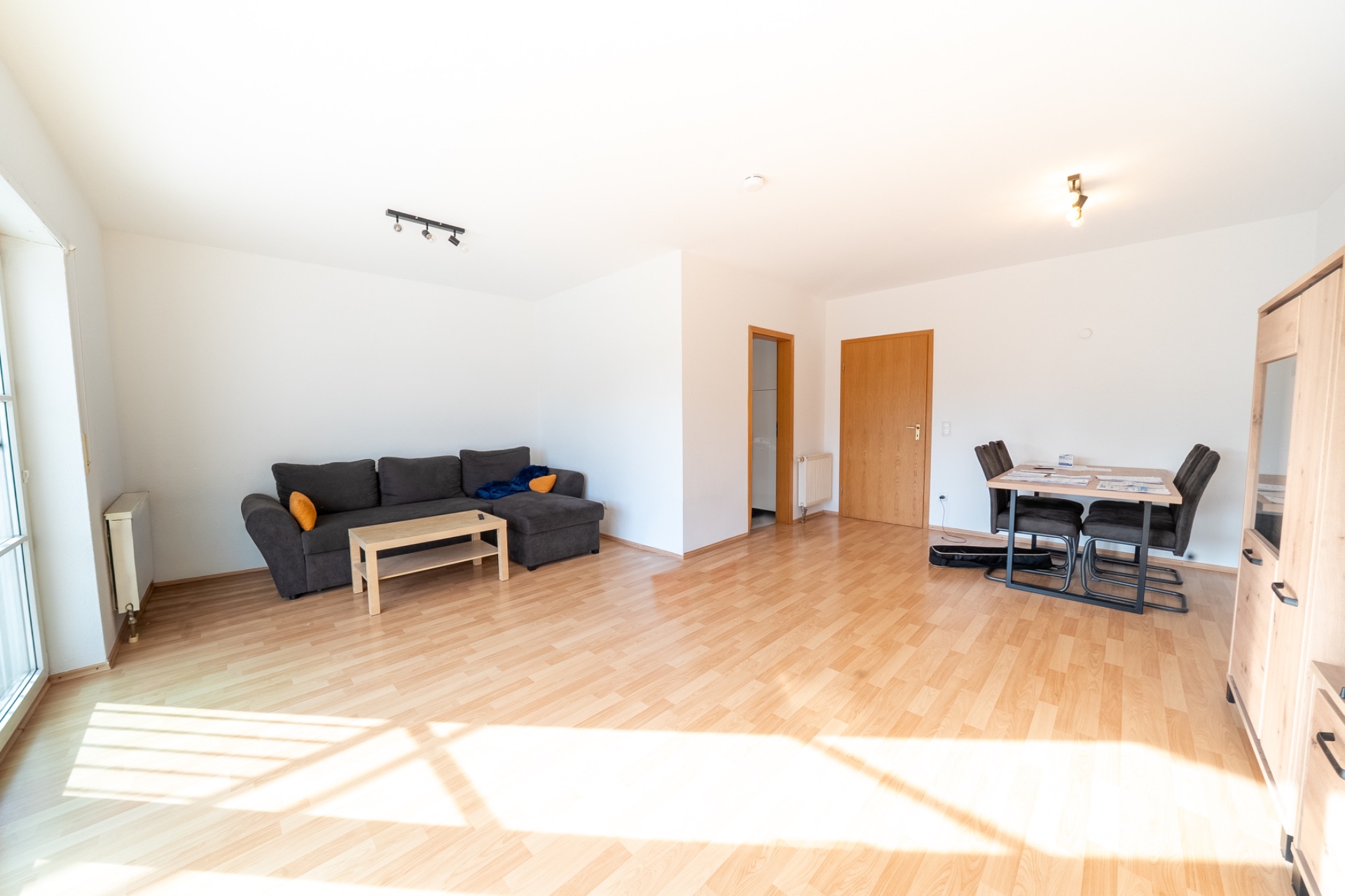 Helles Wohnzimmer mit Holzfußboden, Sofa, Couchtisch und Esstisch mit Stühlen.