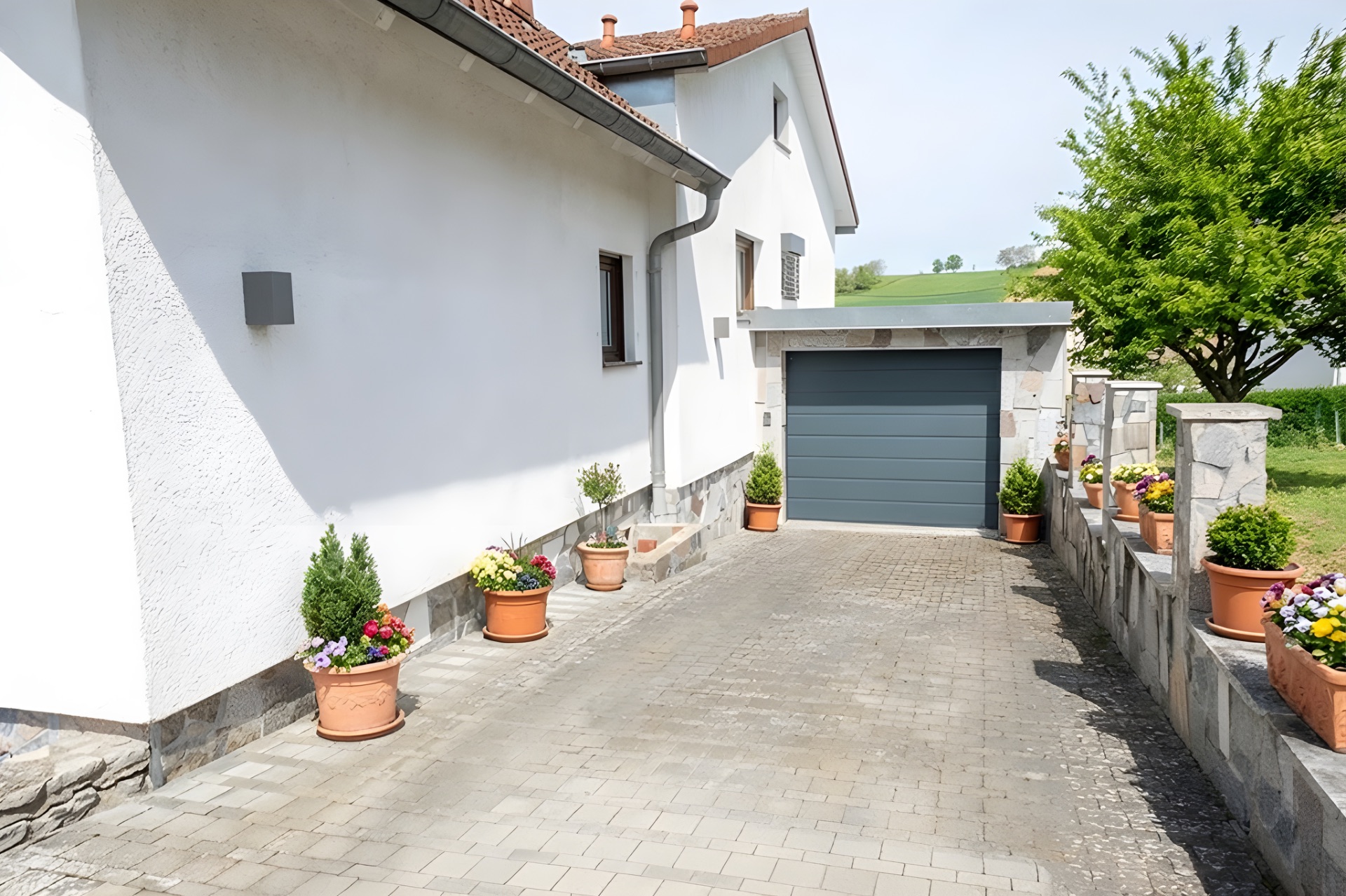 Gepflasterte Einfahrt mit Blumenkübeln führt zu einer Garage an einem weißen Wohnhaus.