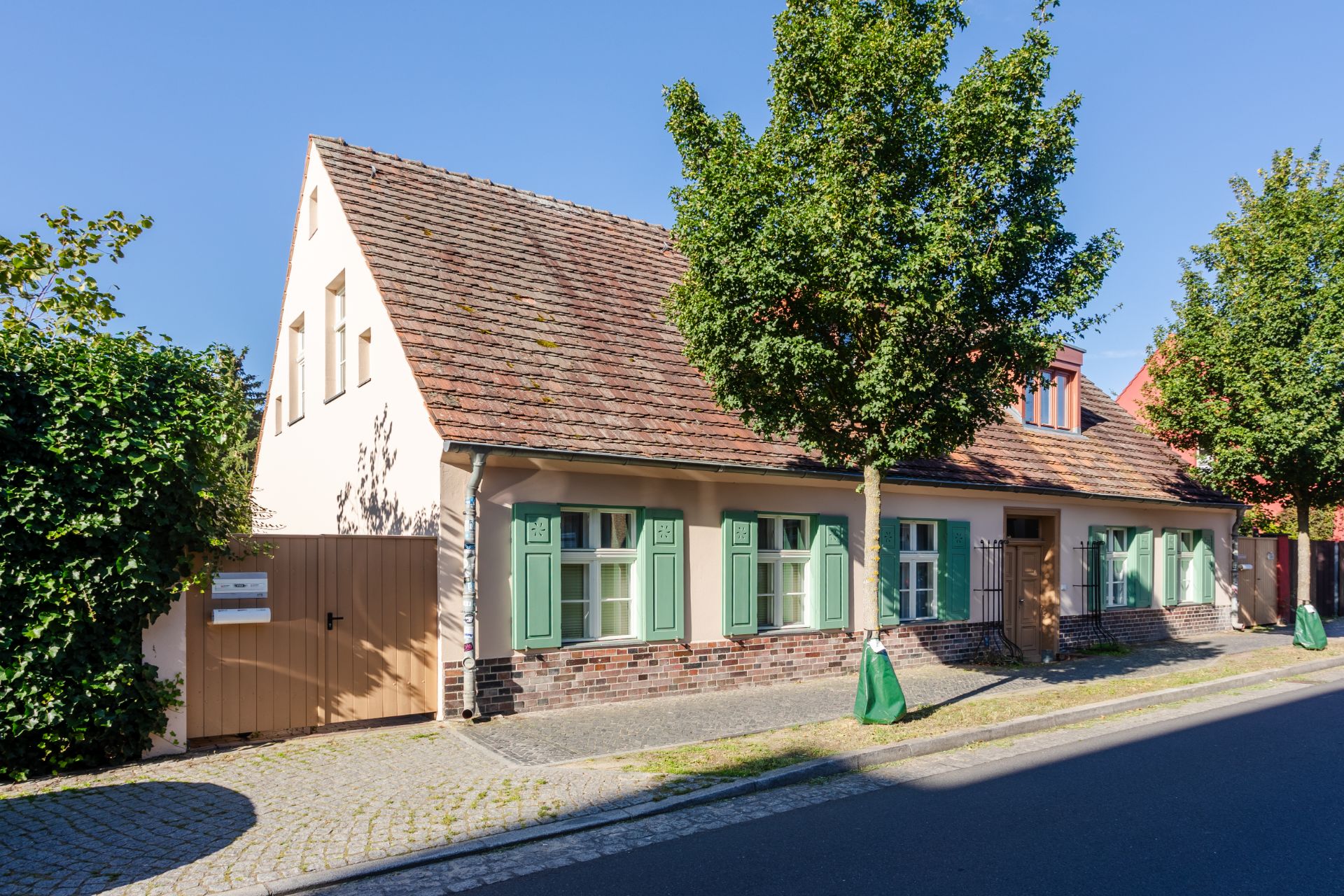 Einfamilienhaus mit grün gestrichenen Fensterläden und Vorgarten an einer ruhigen Straße.
