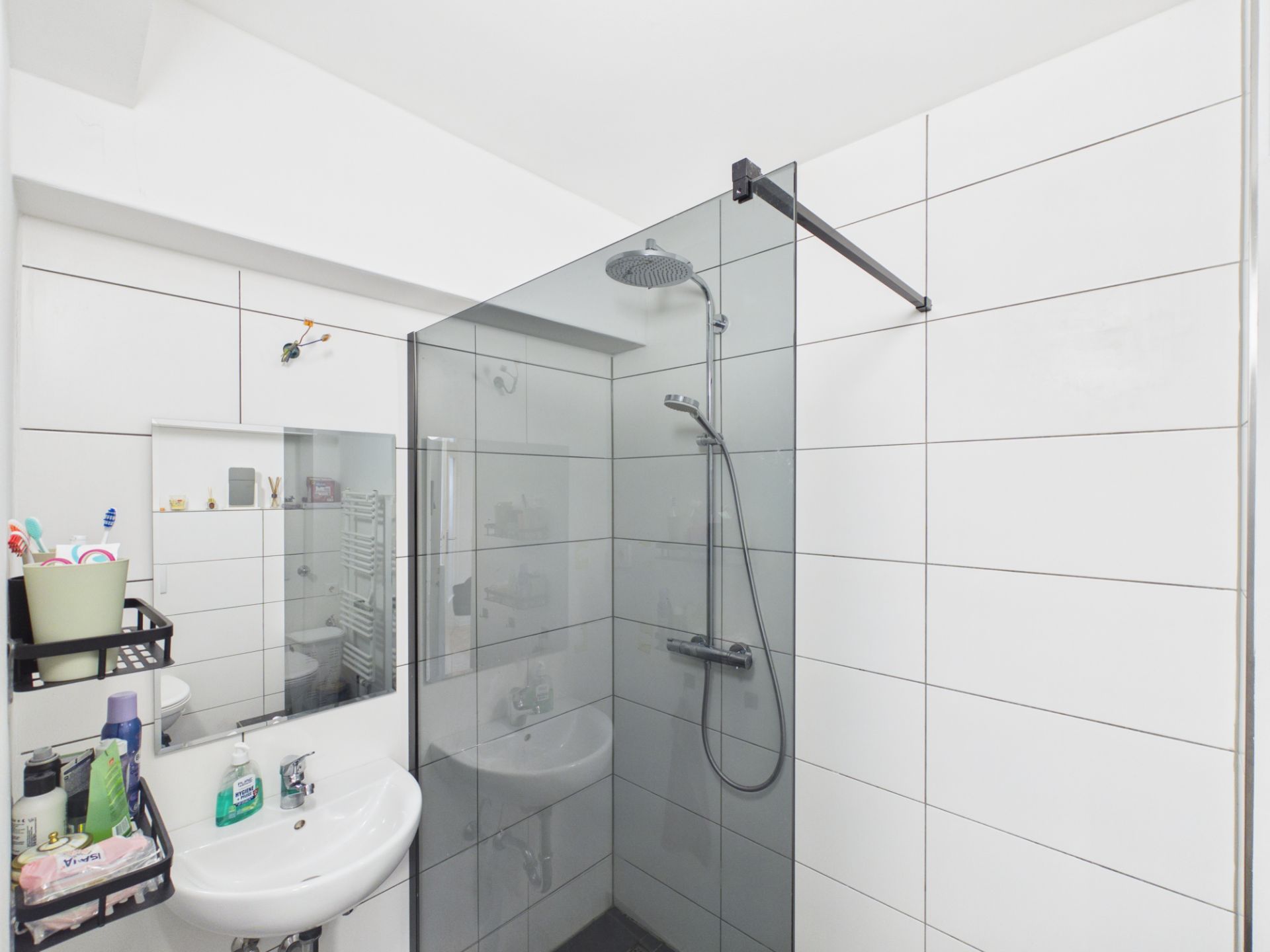Modernes Bad mit Glasdusche, weiß gefliesten Wänden und Waschbecken mit Spiegel.