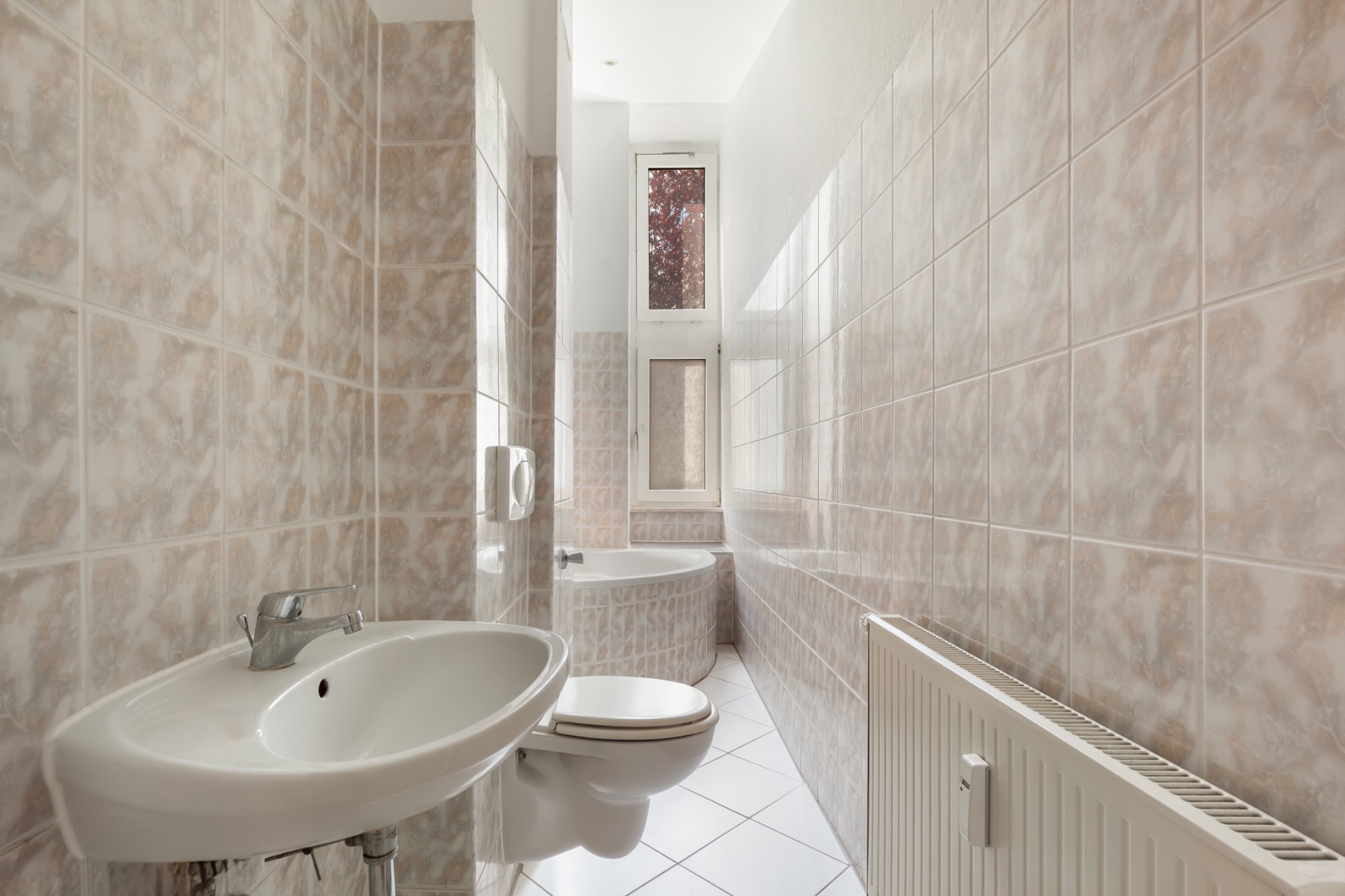 Schmales Badezimmer mit Waschbecken, Wandtoilette, Badewanne und zwei Fenstern.
