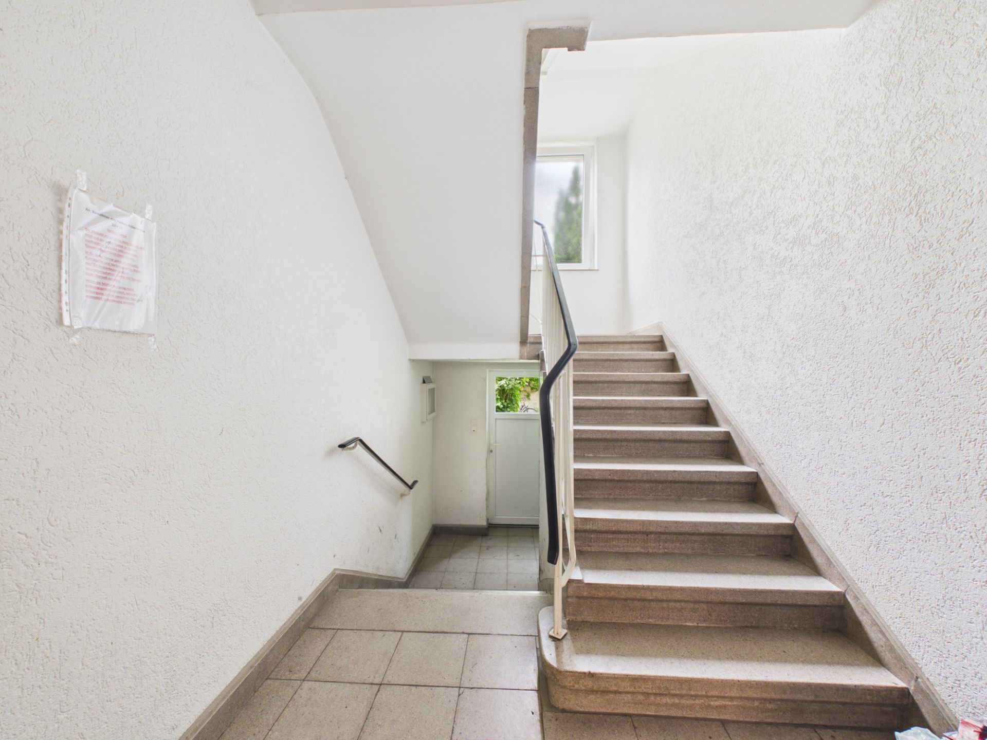 Helles Treppenhaus mit Pflasterfliesen und Fenster am oberen Ende.