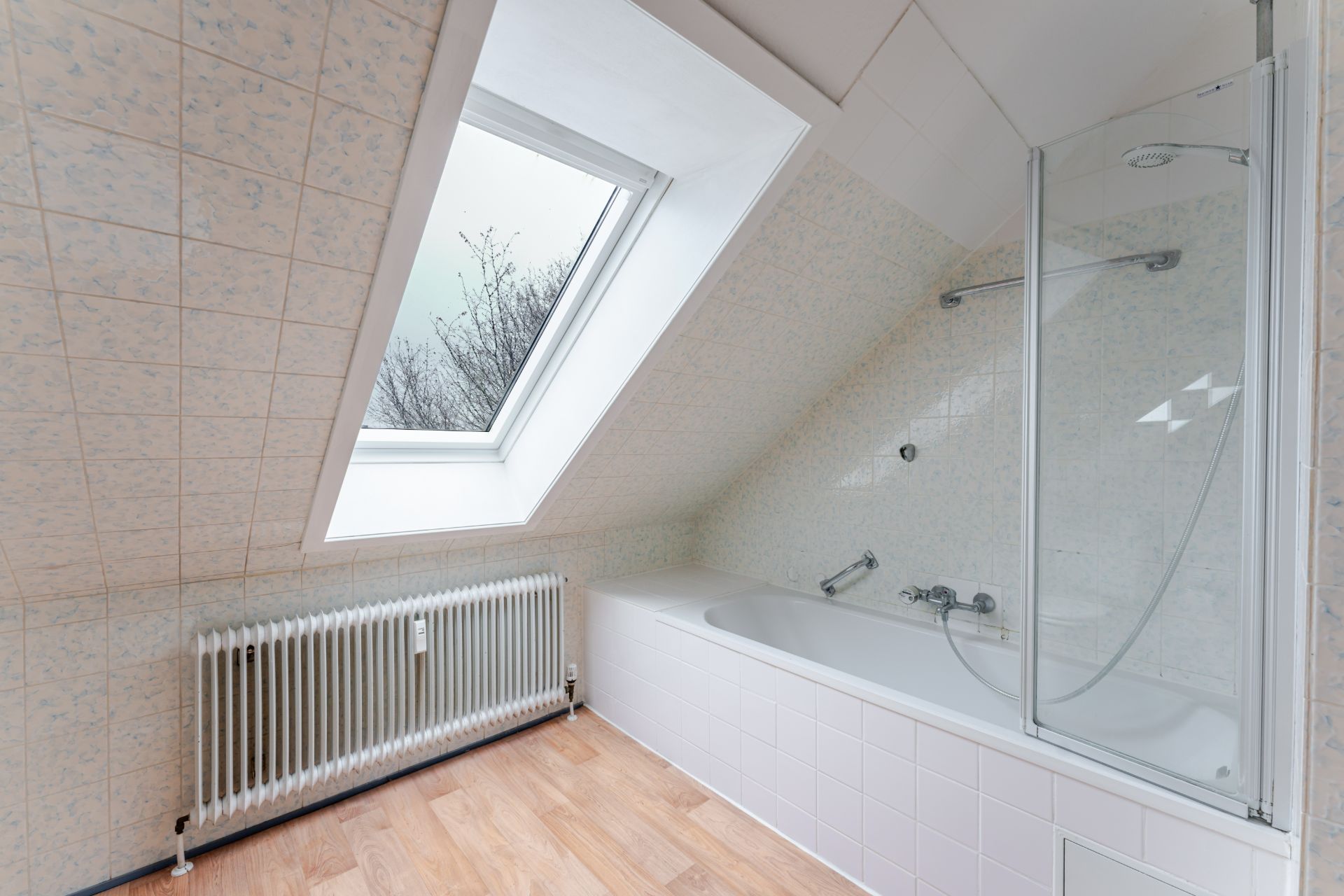 Badezimmer mit Badewanne, Dachfenster und Heizkörper unter einer schrägen Decke.