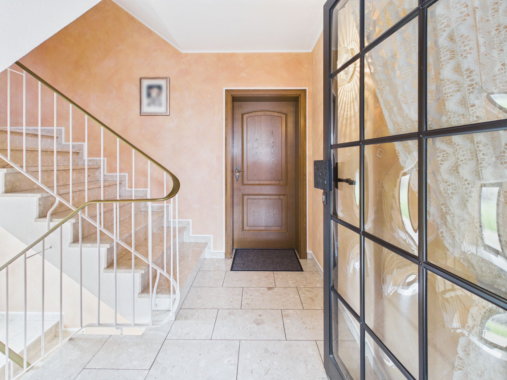 Heller Flur mit Marmortreppe, brauner Tür und gefliestem Boden.