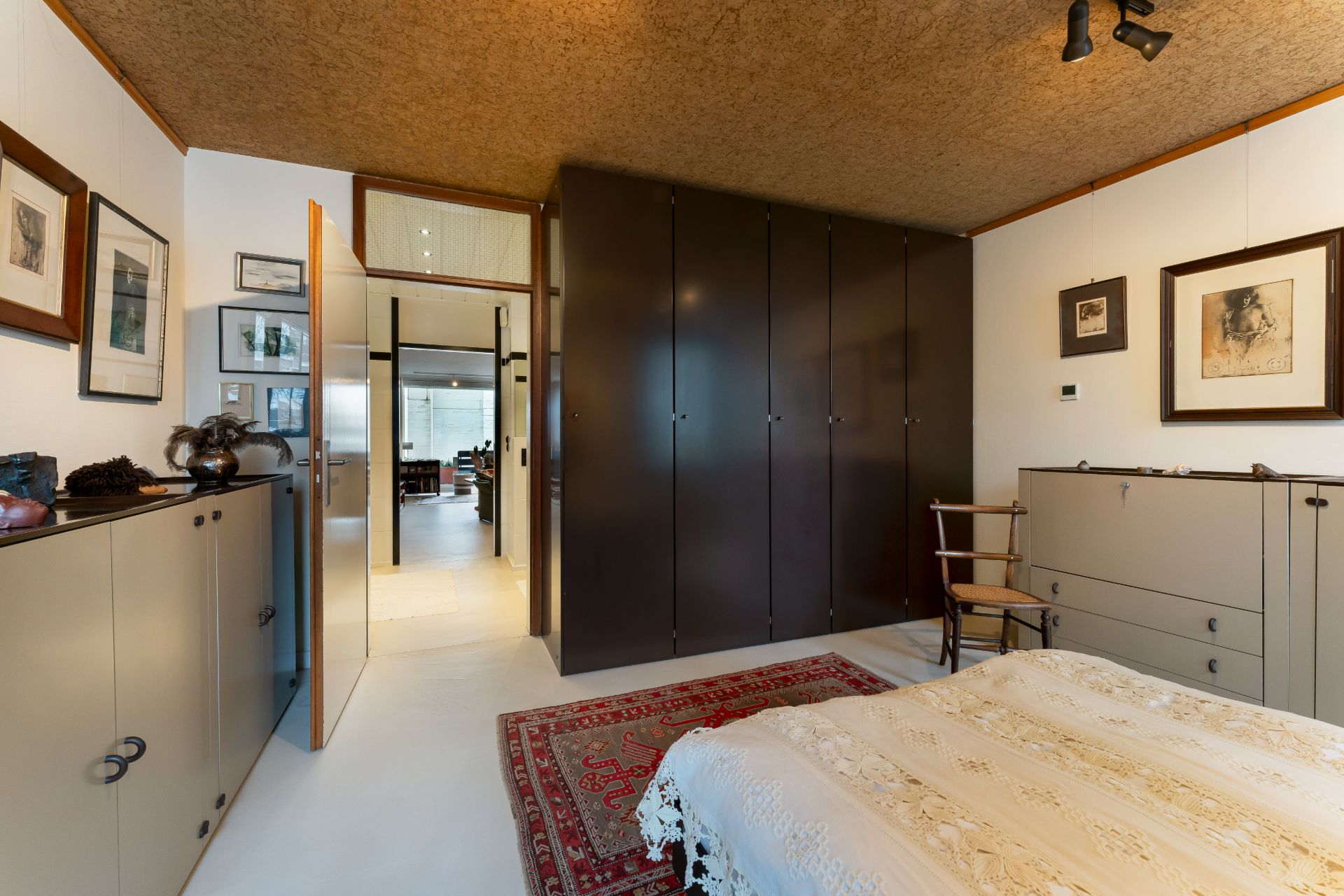 Schlafzimmer mit großem Kleiderschrank, Teppich, Kommode, Bett und dekorierten Wänden.