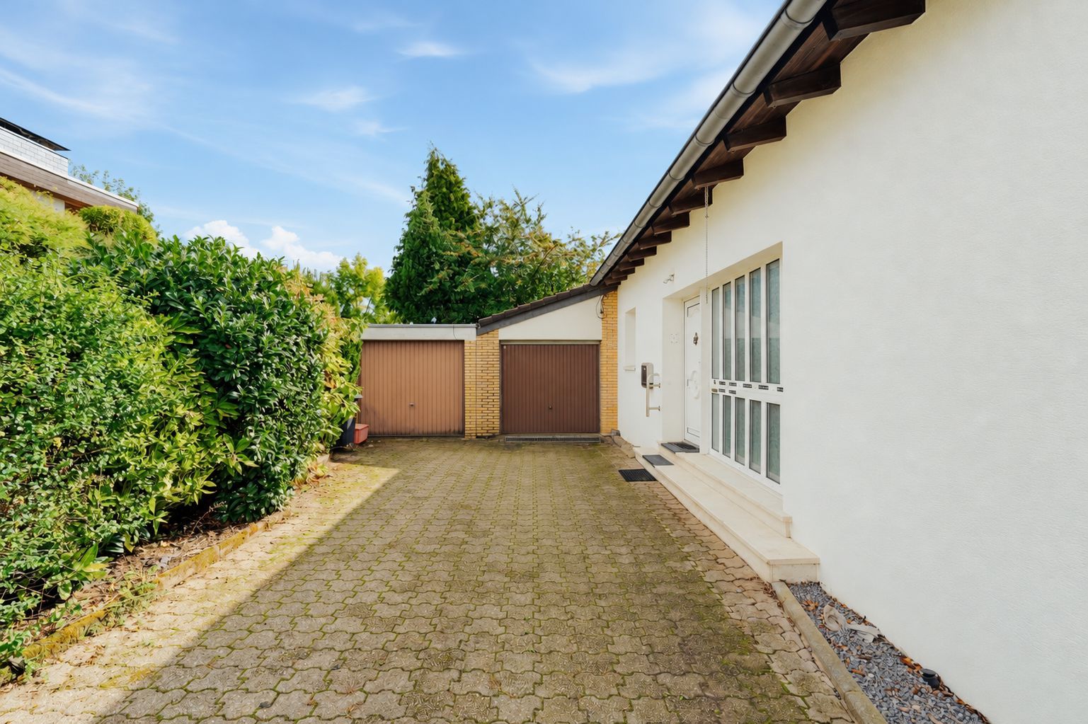 Gepflasterte Einfahrt mit zwei Garagentoren neben einem weißen Wohnhaus.