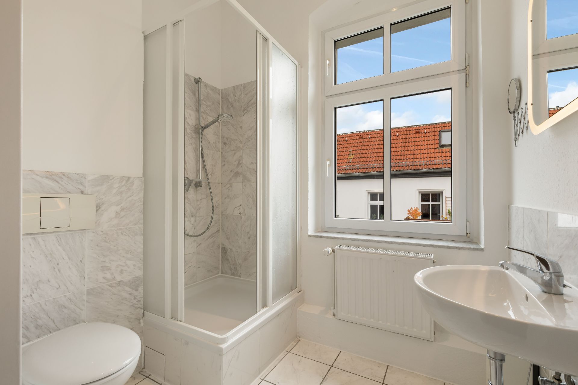 Helles Badezimmer mit Dusche, Toilette, Waschbecken und Fenster.