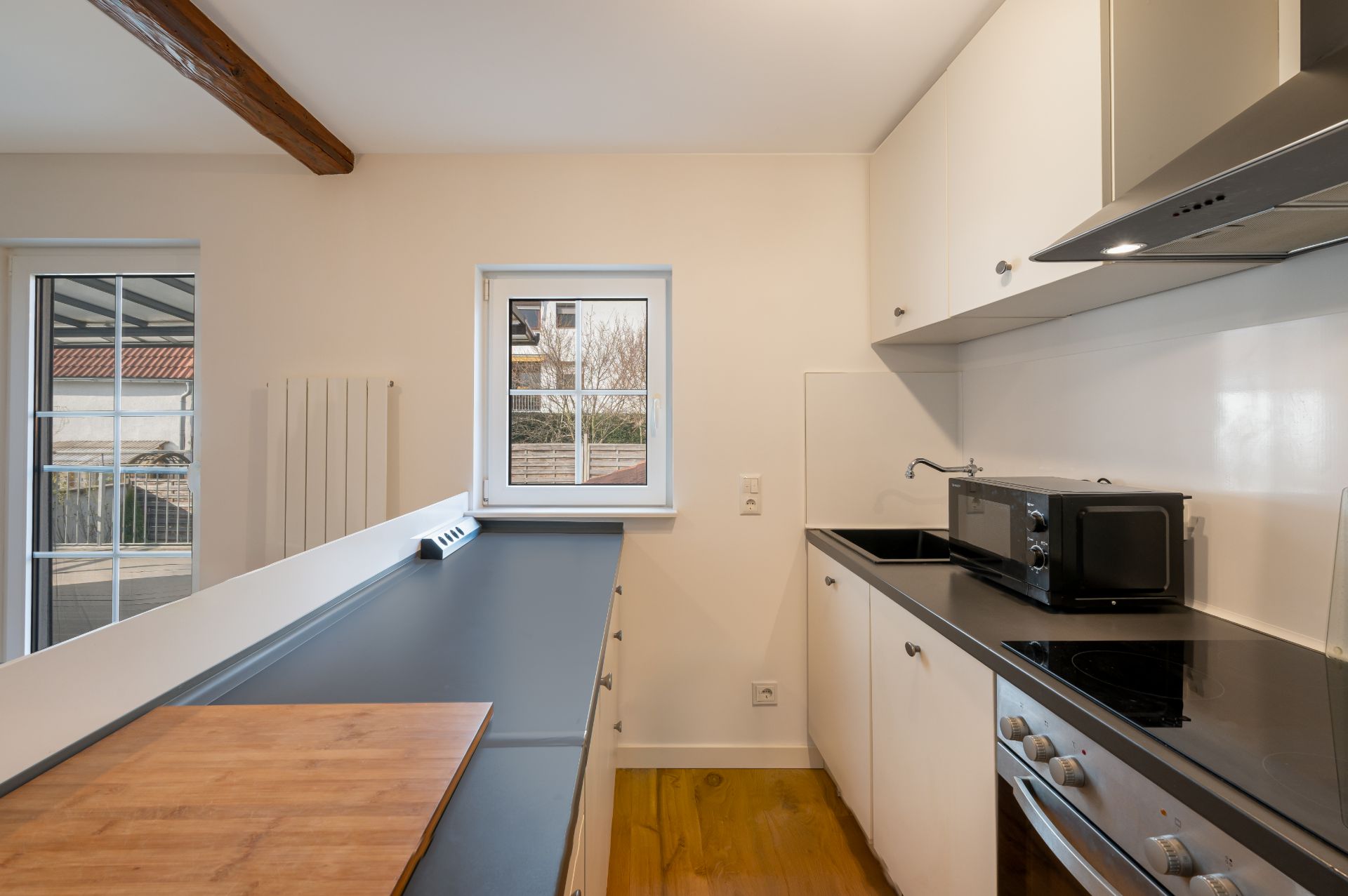Moderne Küche mit weißen Schränken, Herd, Spüle, Mikrowelle und kleinem Fenster.