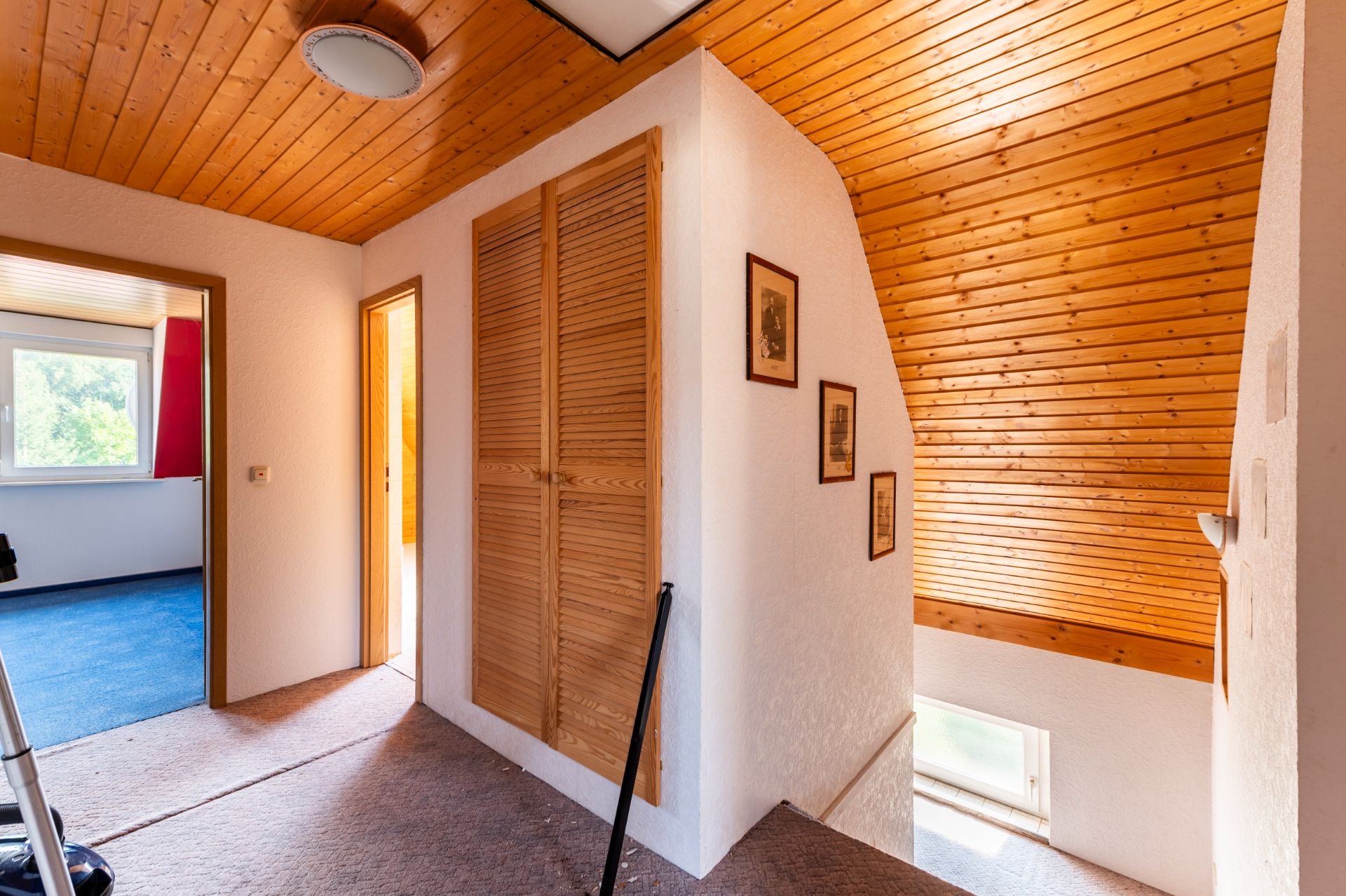 Flur mit Holzdach, Einbauschrank, Bildern an der Wand und Zugang zu Zimmern.