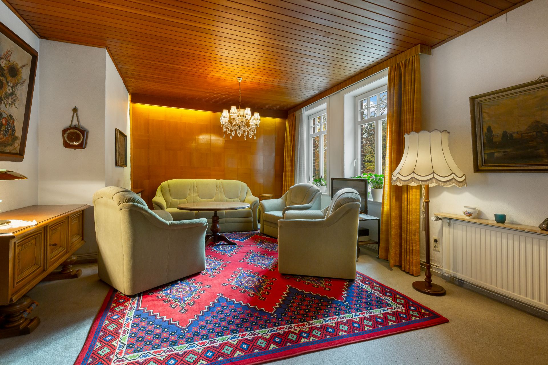 Wohnzimmer mit grünem Sofa, Sesseln, rotem Teppich, Kronleuchter und Stehlampe.