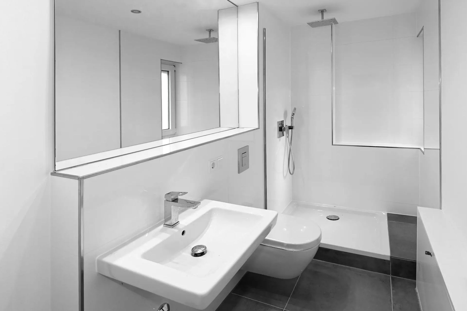 Modernes Bad mit Waschbecken, wandhängender Toilette, Dusche und großem Spiegel.