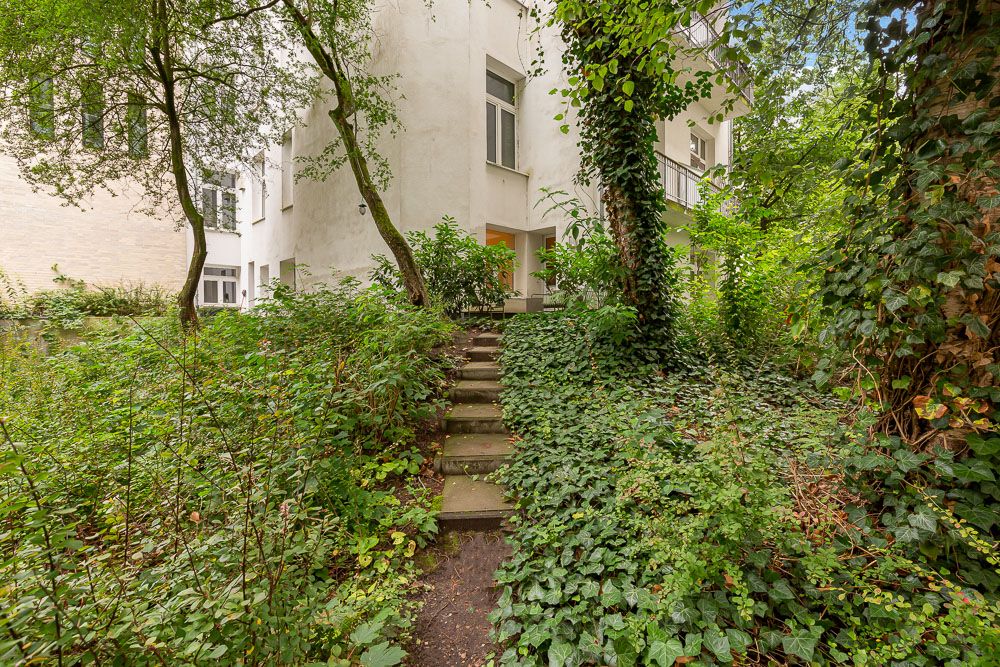 Steintreppe führt durch einen grünen Garten zu einem Hauseingang mit weißen Wänden.