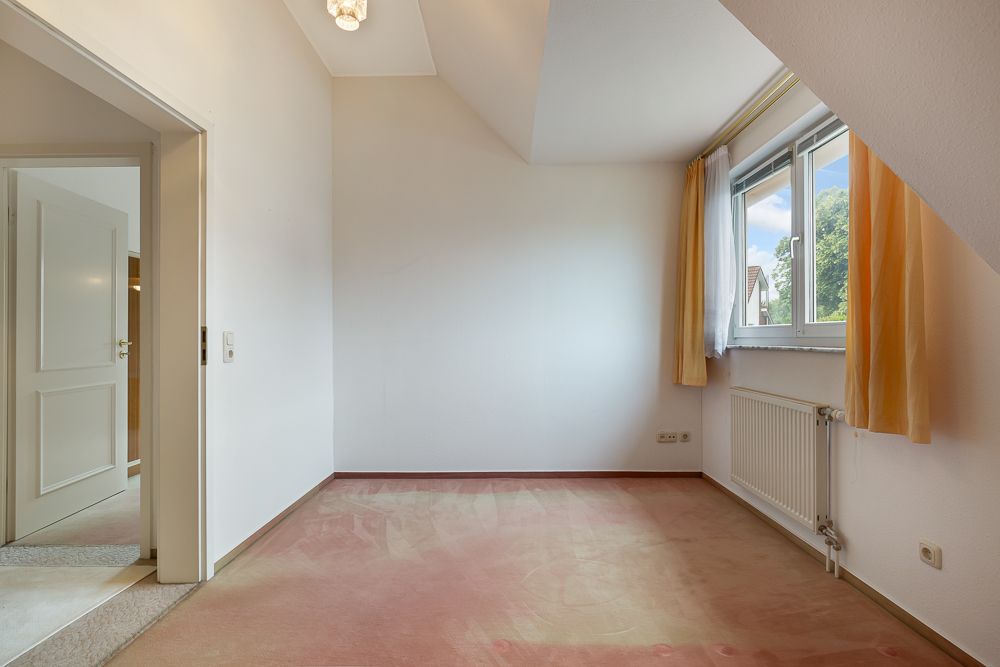 Leeres Zimmer mit Teppichboden, Fenster mit Vorhängen und Heizkörper unter dem Fenster.