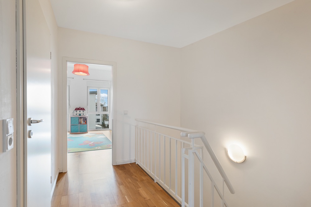 Heller Flur mit Holzfußboden und Blick in ein Kinderzimmer mit bunzem Teppich.