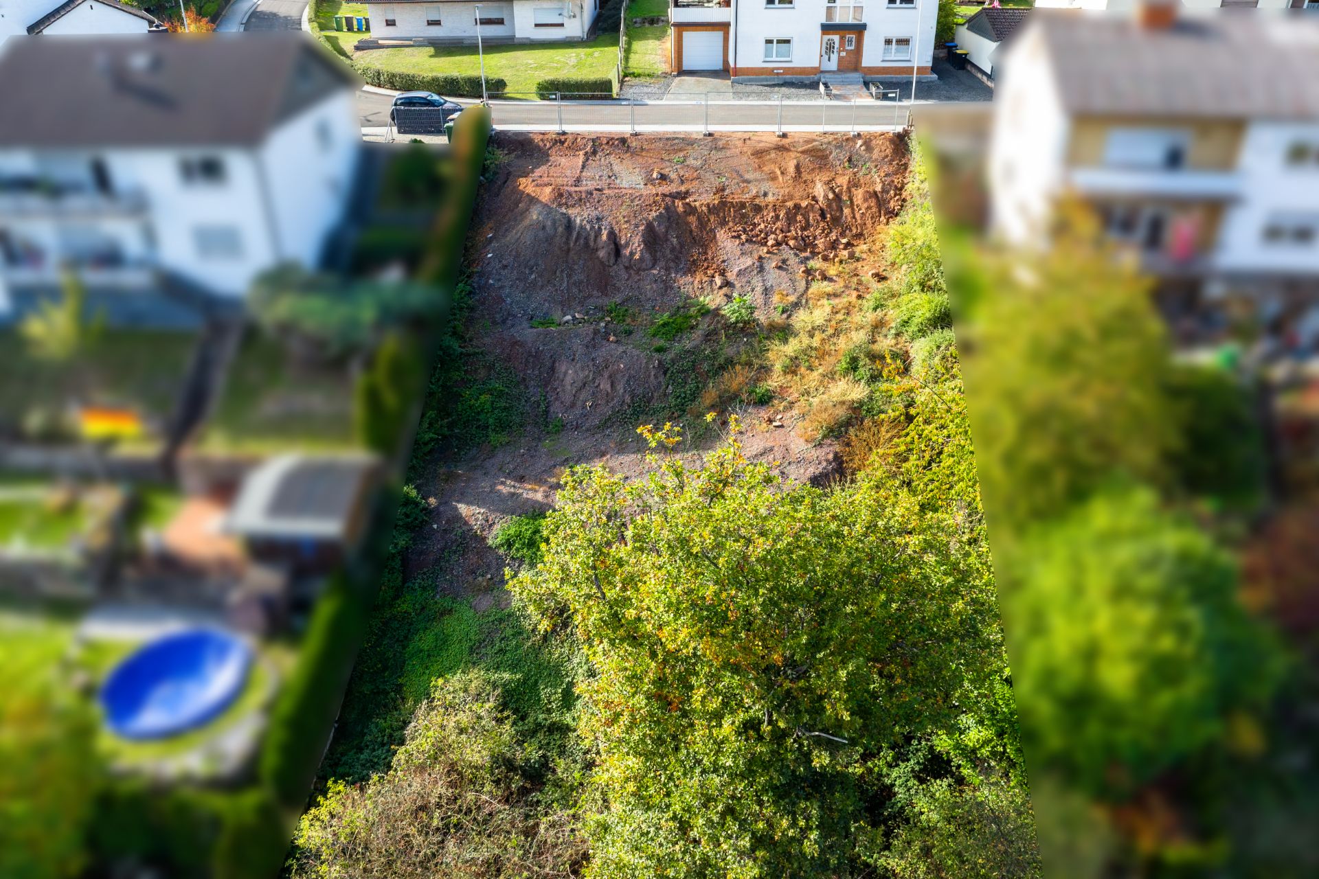Großer Erdrutsch zwischen zwei Wohnhäusern, mit Blick auf eine unbefestigte Böschung und Bäume.