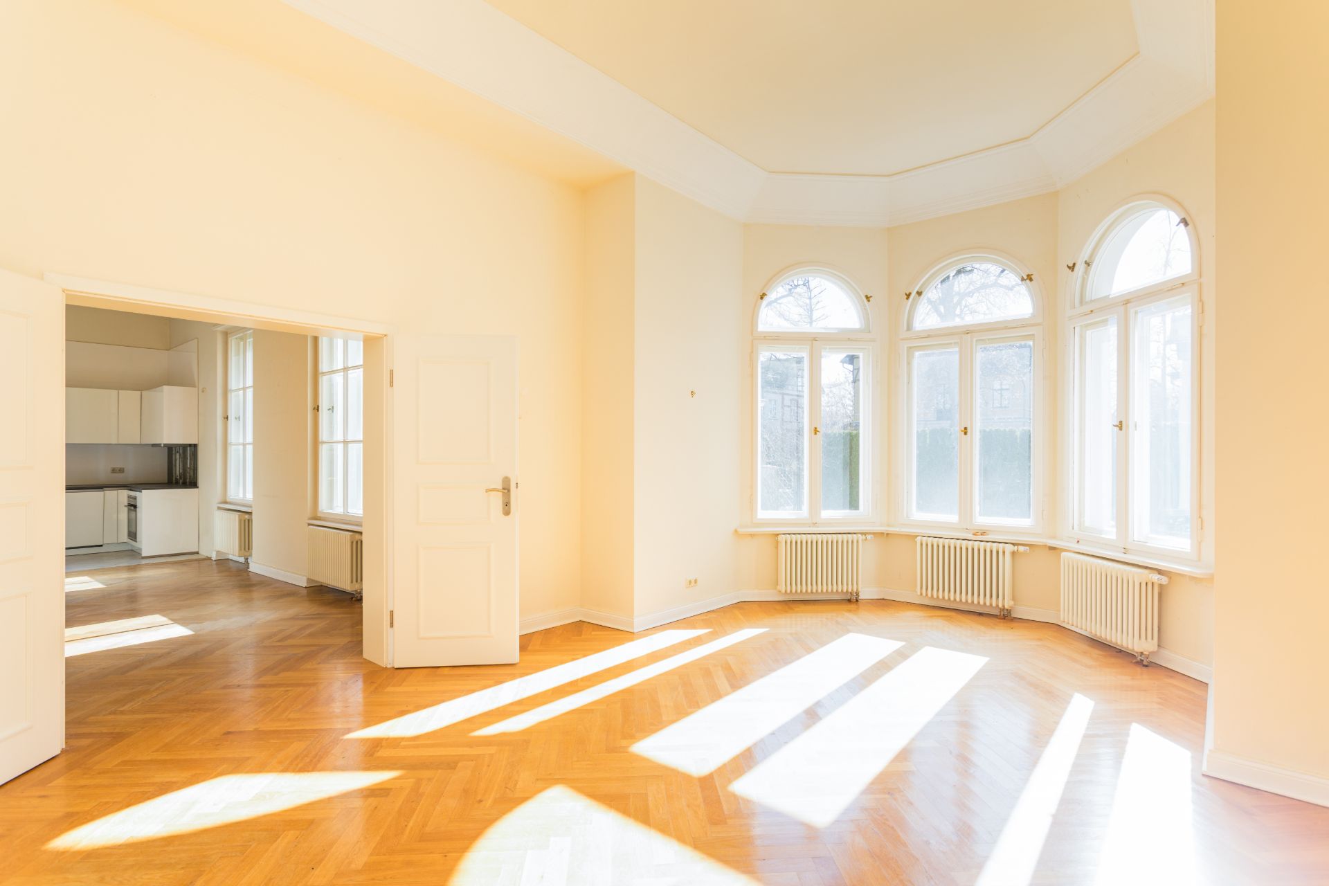 Helles Wohnzimmer mit großen Fenstern, Holzfußboden und Zugang zu einer offenen Küche.