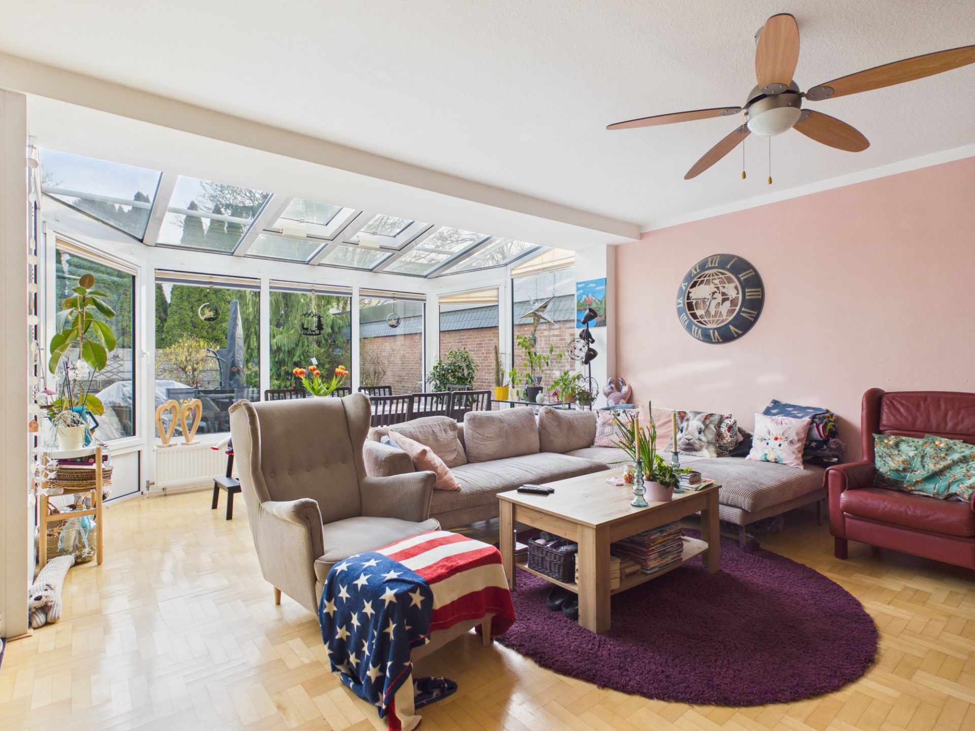 Helles Wohnzimmer mit Ecksofa, Sessel, Couchtisch und großen Fenstern zum Wintergarten.