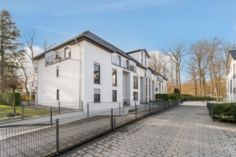 Modernes, weißes Mehrfamilienhaus mit Balkonen und umzäuntem Grundstück bei Tageslicht.