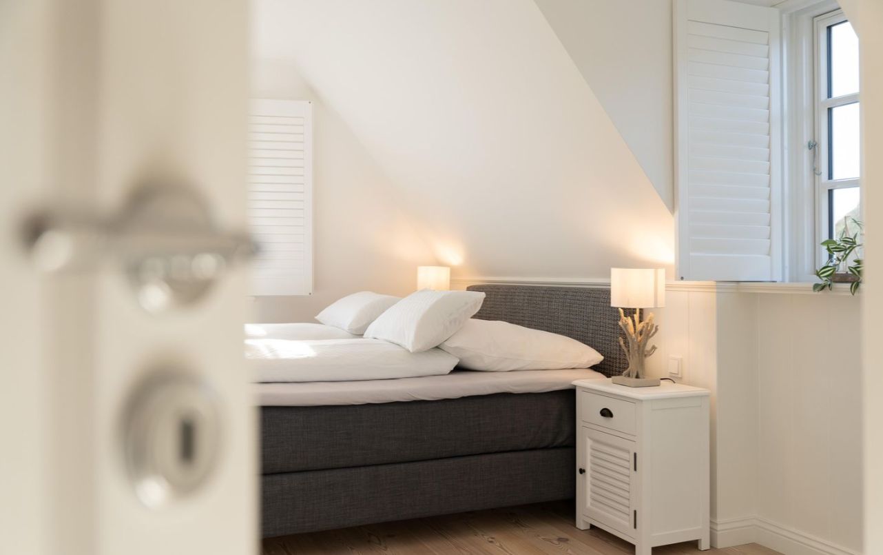 Helles Schlafzimmer mit Doppelbett, zwei Nachttischen und Tischlampen, Fenster mit weißen Jalousien.