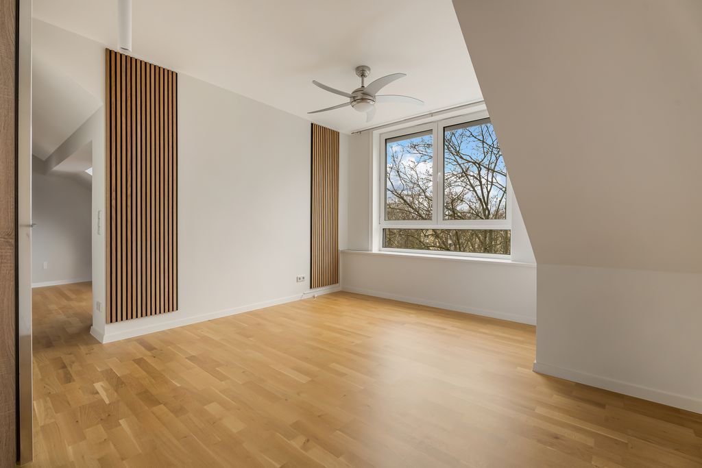 Helles Zimmer mit Holzboden, zwei großen Fenstern und Deckenventilator.