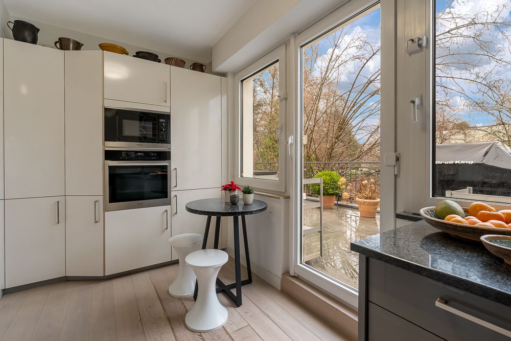 Moderne Küche mit weißen Schränken, Essbereich und Zugang zur Terrasse mit Pflanzen.