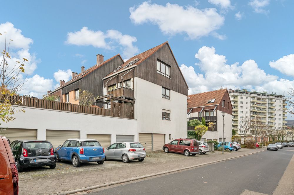 Mehrere Wohnhäuser mit Garagen und parkenden Autos an einer ruhigen Straße.