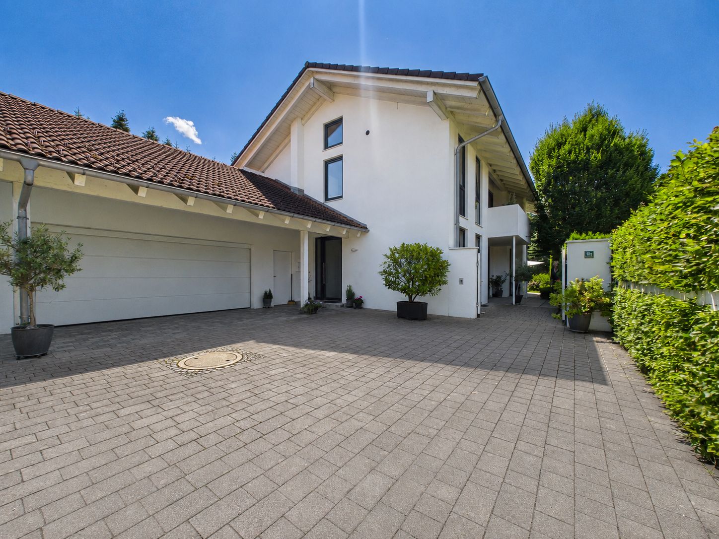 Modernes weißes Wohnhaus mit Garage, gepflasterter Einfahrt und Pflanzen.