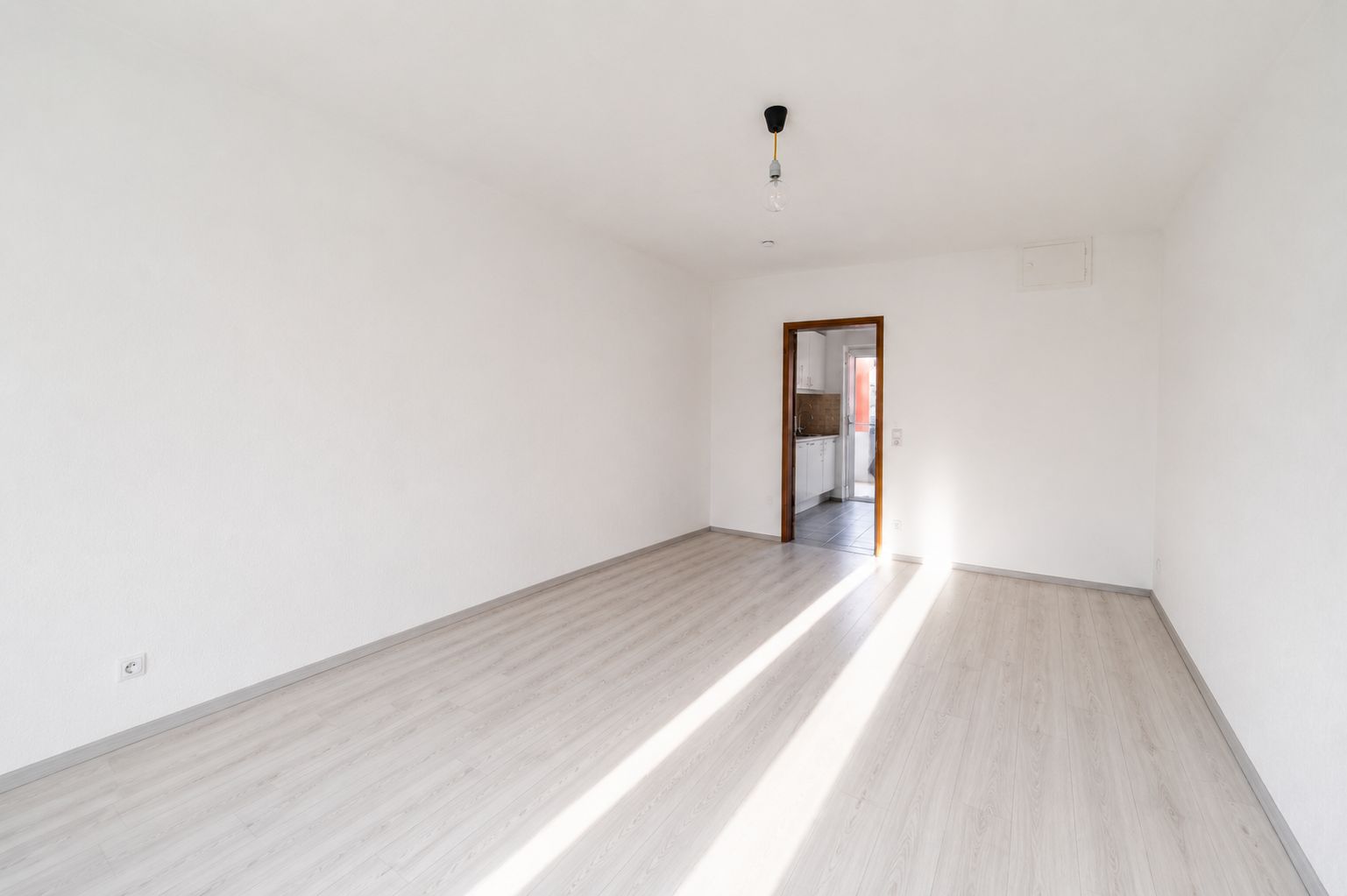 Helles, leeres Zimmer mit weißem Boden und Decke, Tür öffnet zu weiterem Raum.