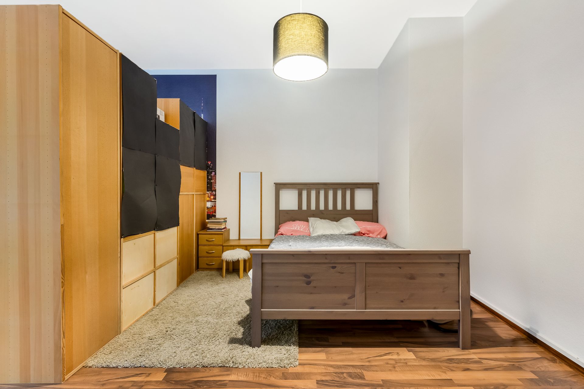 Schlafzimmer mit Holzbett, Kleiderschrank, Nachttisch und Lampe an der Decke.