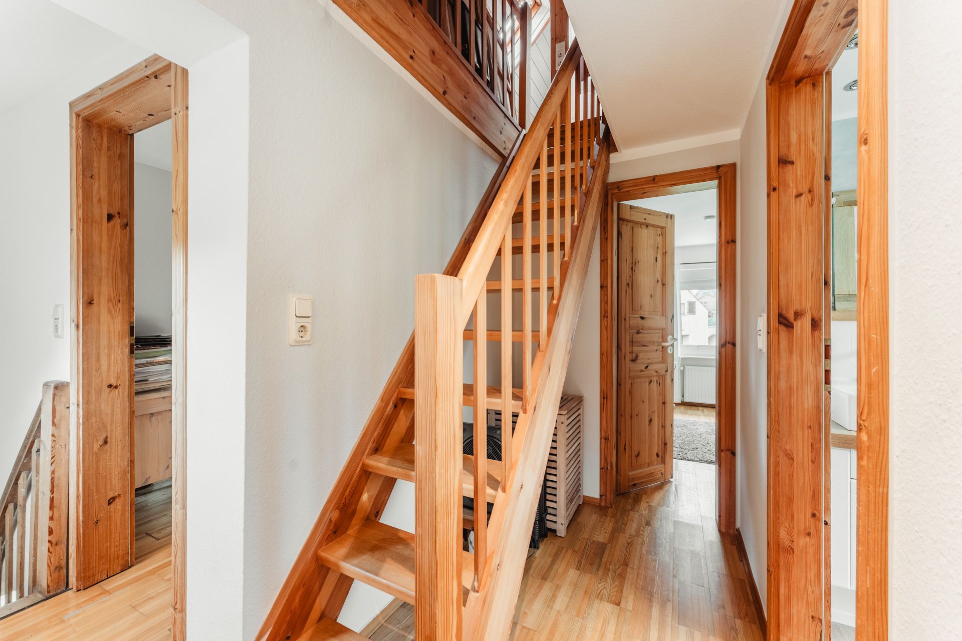 Helle Diele mit Holztreppe, Holztüren und Holzfußboden in einem Wohnhaus.