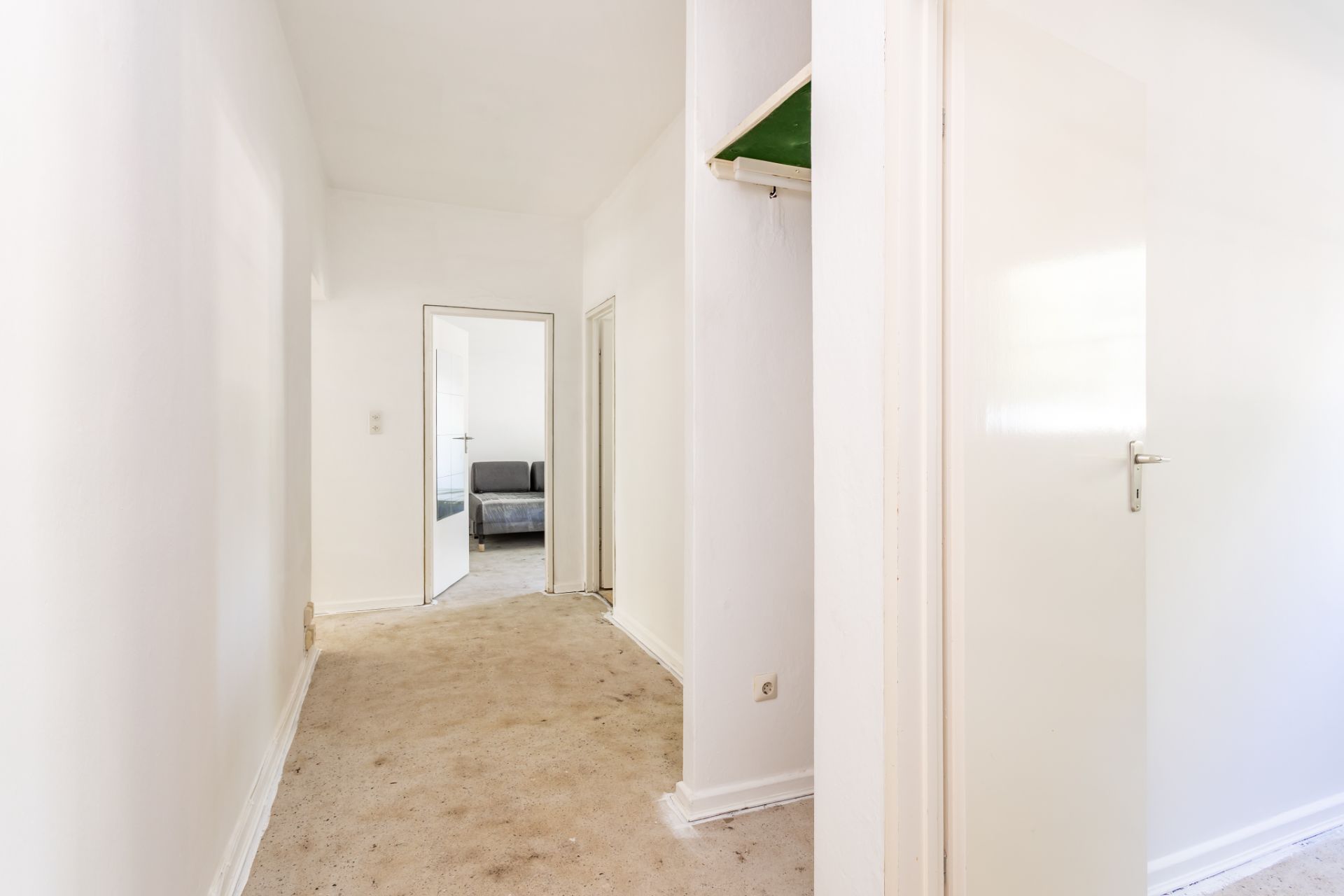 Heller Flur mit Teppich, weißen Wänden und Türen, im Hintergrund ein Raum mit Sofa.