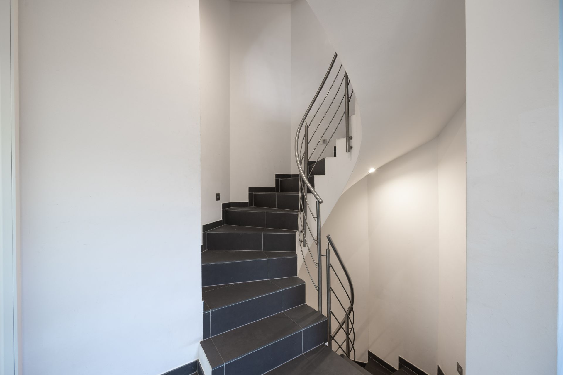 Moderne Treppe mit dunklen Fliesen und Metallgeländer in einem hellen Flur.