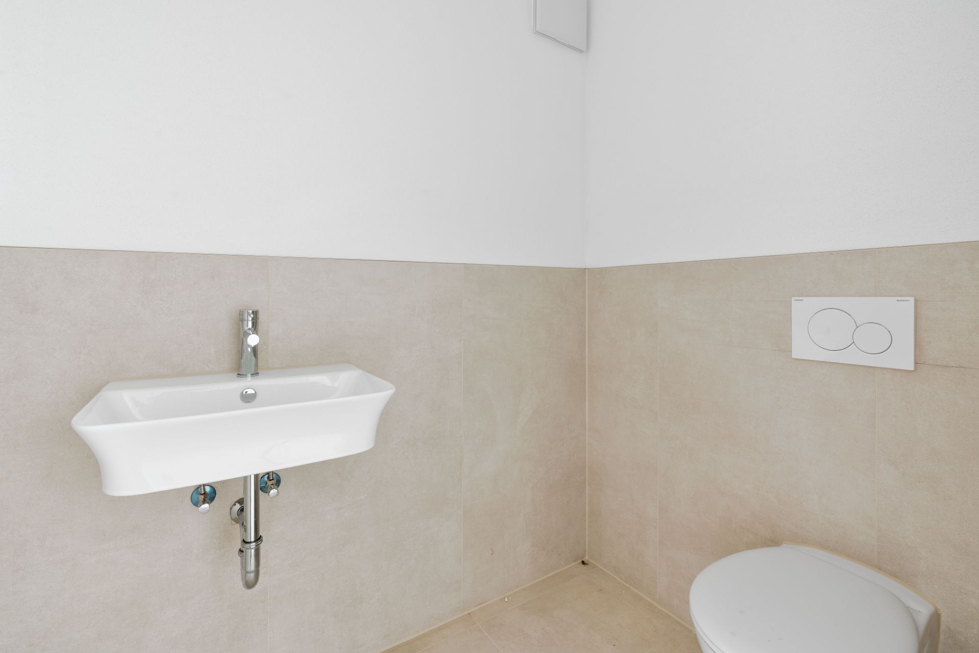 Heller, minimalistischer Waschraum mit Waschbecken und Toilette an hellen Fliesenwänden.