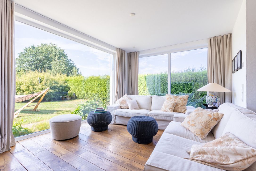 Helles Wohnzimmer mit Sofas, Holzboden, großen Fenstern und Blick in den Garten.