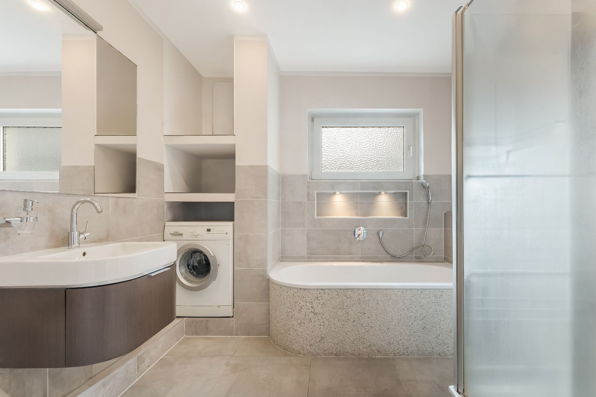 Modernes Badezimmer mit Waschmaschine, Badewanne, Dusche, Waschbecken und Fenster.