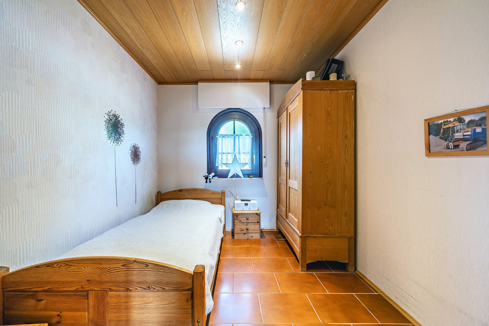 Kleines Schlafzimmer mit Einzelbett, Holzschrank, Nachttisch und rundem Fenster.